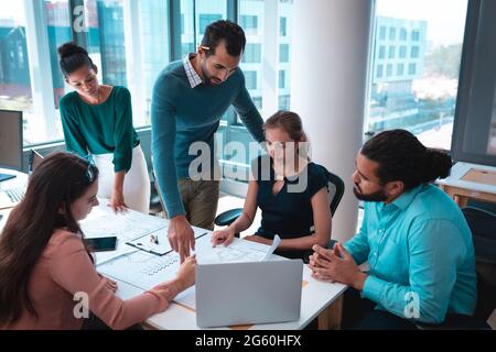 Group of diverse businesspeople discussing together sitting at table and using laptop Stock Photo