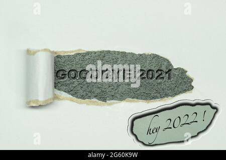 Text Goodbye 2021 appearing behind torn white paper. top view of open white paper and the message 2021 written behind on dark background. And hey 2022