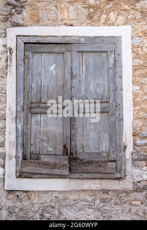 Old window wooden shutters closed, stone wall building facade. Abandoned house at Naflion old town, Greece. Vertical view. Stock Photo
