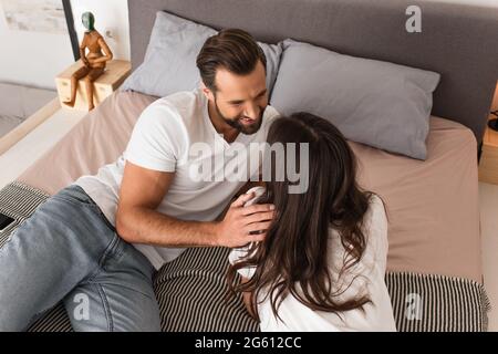 Overhead view of cheerful man hugging girlfriend while resting on bed Stock Photo