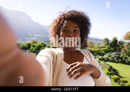 Happy african american woman on sunny balcony of country home making video call, smiling Stock Photo