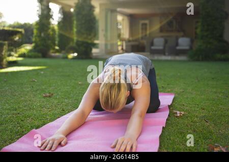 Caucasian woman practicing yoga in garden, kneeling and stretching Stock Photo