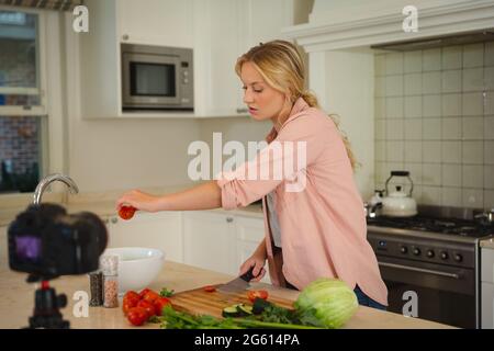 Caucasian woman in kitchen preparing food and using camera, making cooking vlog Stock Photo