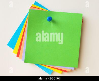 Colorful Paper Notes Stacked Together And Pinned On The Wall. Different Colored Sheets Of Note Attached On A Plain Wallpaper With A Pin. Stock Photo