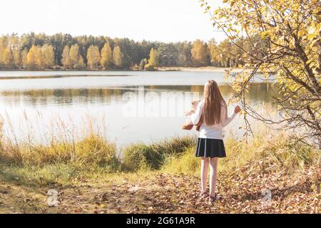 Blonde girl holds bear looking at river in autumn forest Stock Photo