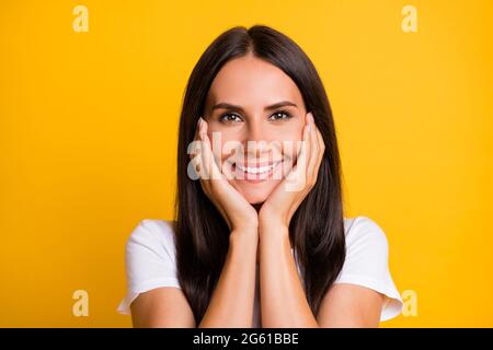 Photo of cute dreamy young lady wear white t-shirt arms cheeks isolated yellow color background Stock Photo