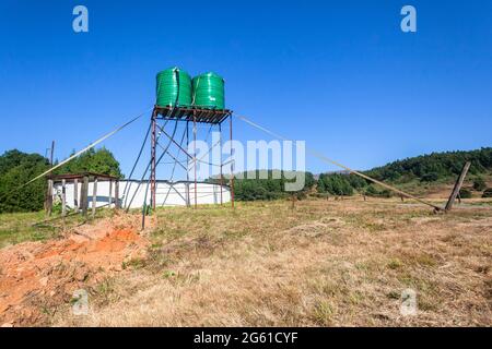 Forest Farm with two Large green colored water tanks on tall steel stand above round reserviour place in open field in blue sky landscape. Stock Photo