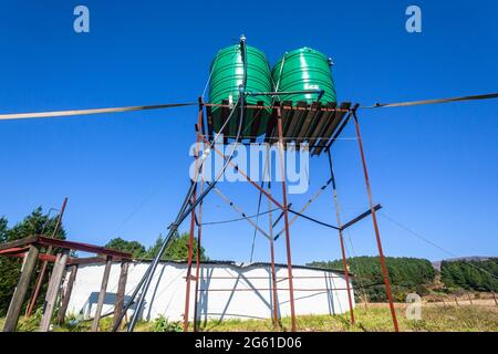 Forest Farm with two Large green colored water tanks on tall steel stand above round reserviour place in open field in blue sky landscape. Stock Photo