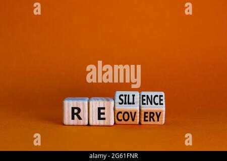 Recovery and resilience symbol. Turned wooden cubes and changed the word 'recovery' to 'resilience'. Beautiful orange background. Business and recover Stock Photo