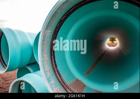 Stacked water main pipe with bell fitting next to an exposed trench for installation Stock Photo