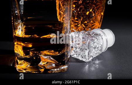 Close-up of a crystal glass along with a bottle full of whiskey on black background. Coktails and spirits Stock Photo