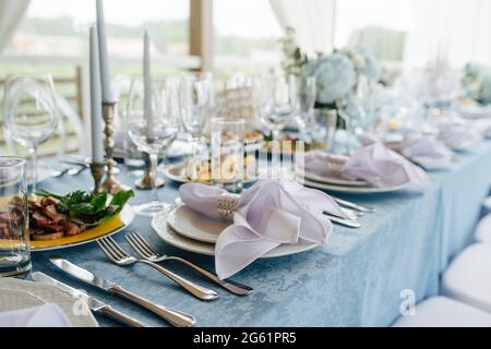 Long abundant table set for an event on a terrace. Empty plates and glasses and some appetizers in between. Low angle. Stock Photo