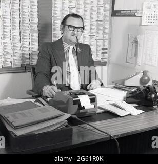 1970s, historical, inside an office, sitting at his desk, parker pen in hand and smoking a pipe, a suited executive working in auto finance, with two telephones, paperwork and a mechanical adding machine around him, Croydon, England, UK. A walled customer/supplier card index is on the wall behind him. The financing of motor cars is big business. GMAC, an acronym for General Motors Acceptance Corporation was founded in 1919 and was part of the US car giant, General Motors, who owned the Vauxhall car brand in the UK, which they had acquired in 1925. Stock Photo