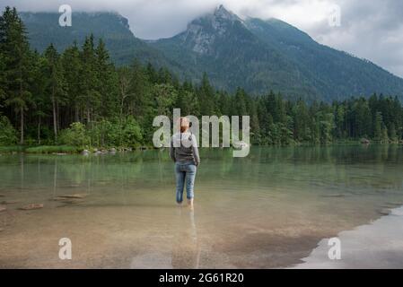 Young woman standing at lakeside of beautiful mountain lake in Bavaria, Germany Stock Photo