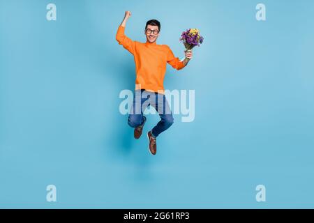 Full size photo of astonished handsome guy jumping fist up hold flowers isolated on blue color background Stock Photo
