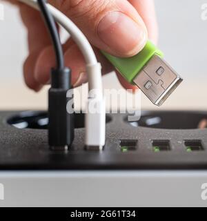 Modern convenient multi-port usb charger for devices. Close-up of a female hand plugging multi-colored cables into a power outlet. Macro. Stock Photo