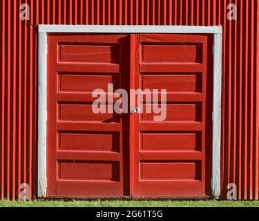 Closed wooden red doors against bright red wooden barn exterior wall Stock Photo