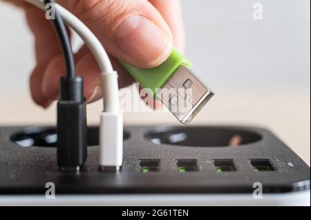 Modern convenient multi-port usb charger for devices. Close-up of a female hand plugging multi-colored cables into a power outlet. Macro. Stock Photo