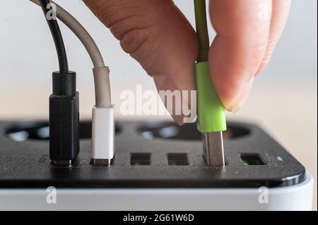 Modern convenient multi-port usb charger for devices. Close-up of a female hand plugging multi-colored cables into a power outlet. Macro. Stock Photo