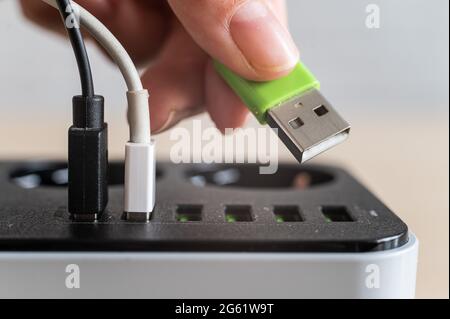 Modern convenient multi-port usb charger for devices. Close-up of a female hand plugging multi-colored cables into a power outlet. Macro. Stock Photo