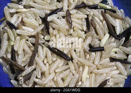 Macro closeup of raw isolated long grain wild  and healthy brown black wholemeal rice in blue bowl Stock Photo