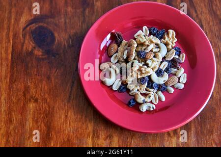 red plate with mixed nuts dried fruits on wooden background from above. Healthy food and snack. Walnut, pistachios, almonds, hazelnuts and cashews. ho Stock Photo