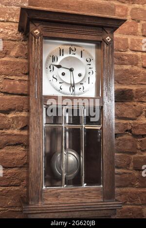 Vintage grandfather clock in wooden body stands near red brick wall. Close up vertical photo Stock Photo