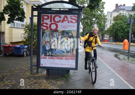 Pablo Picasso exhibition advertising at a bus stop and a young woman with bicycle at Saarstrasse in Berlin, Germany - June 30 2021 - Museum Berggruen in Berlin shows the exhibition 'Picasso & Les Femmes d´Alger' 21.05.2021 to 29.08.2021. Stock Photo