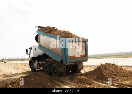 Dump truck unloads clay soil for the construction of a new highway. Clay for laying the foundation of a new road. Stock Photo