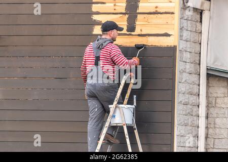 Kiev, Ukraine - April 27, 2021: A man painting wooden wall outside. Stock Photo