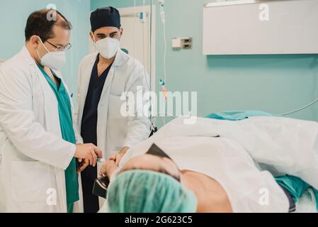 Medical doctor giving patient anesthesia before surgical operation inside modern hospital - Focus on right doctor face Stock Photo