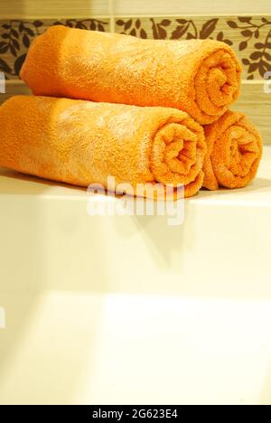 Three orange rolled towels on a ceramic sink in a luxurious and clean bathroom Stock Photo