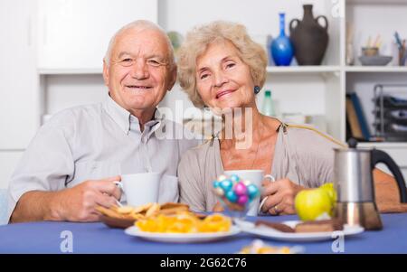 Smiling elderly spouses enjoying tea with sweets Stock Photo