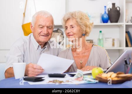 Happy senior spouses with bills and laptop Stock Photo