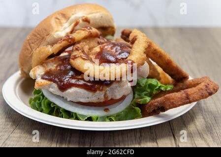 Barbeque chicken sandwich stacked tall in the toasted bun with huge onion rings on the side to fill the entire plate. Stock Photo