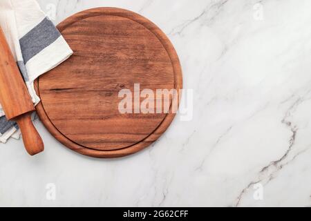 Empty wooden pizza platter with napkin and rolling pin set up on marble stone kitchen table. Stock Photo
