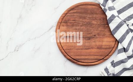 Empty wooden pizza platter with napkin set up on marble stone kitchen table. Pizza board and tablecloth on white marble background. Stock Photo