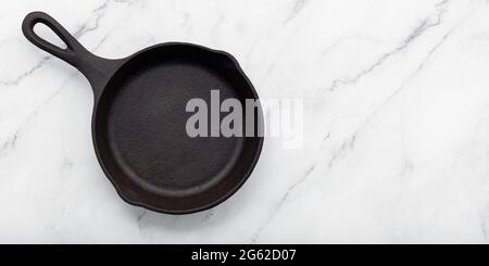 Empty old cast iron skillet set up on white marble  background with flat lay and copy space. Stock Photo