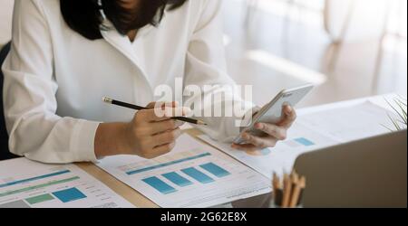 Young woman using smart phone and checking financial report and calculating expenses in the office Stock Photo