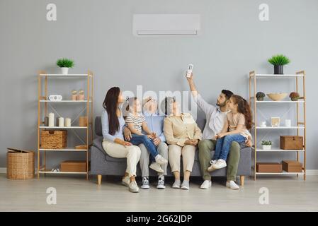 Happy family sitting together on a couch at home under a new modern air conditioner Stock Photo