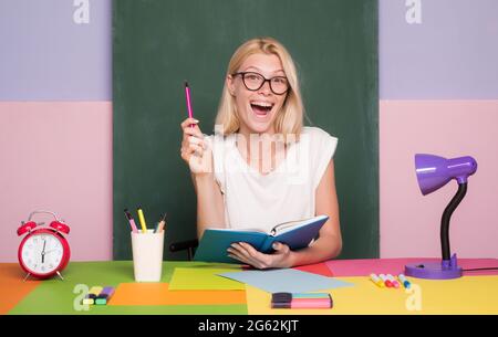 Female teacher at her desk marking students work. Pretty teacher smiling at camera at the school. University student. Female student taking notes from Stock Photo
