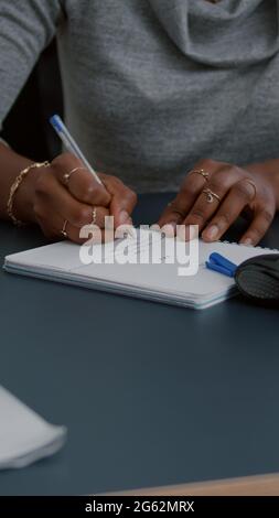Closeup of student with black skin writing communication homework on notebook while sitting at desk in living room. Young woman studying math on elearning platform doing homework during high school Stock Photo