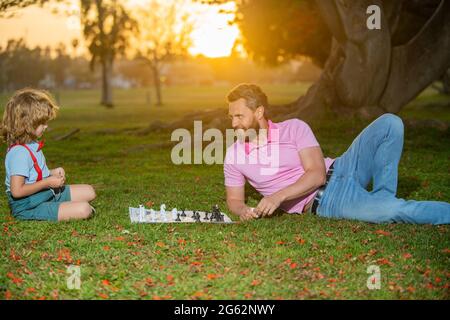 Happy family outdoor. Father and son playing chess in summer garden. Little boy play chess with parent. Cognitive development. Intellectual kids game Stock Photo