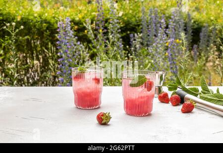 Cold, strawberry mocktail or cocktail with mint, ice cubes in front of the garden. Stock Photo