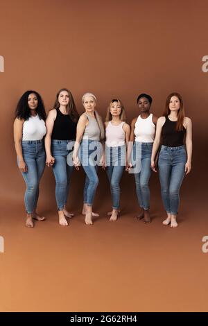 Six diverse women holding hands. Group of multi ethnic females of different ages looking at camera. Stock Photo