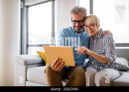 Lovely smiling mature couple having fun while using tablet at home Stock Photo
