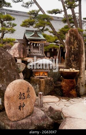 A Shinto shrine on the Japanese Island of Miyajima with a wooden miniature shrine and cleansing water station. Stock Photo