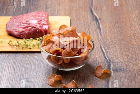 Selective focus on jerky in a glass bowl on a wooden background. Blurred beef with thyme on a cutting board. Stock Photo