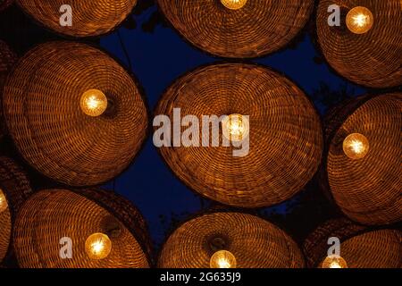Many wicker lighted lamps hang by background of dark night sky. Lot of hanging electrical lantern, festive decor in evening yard Stock Photo