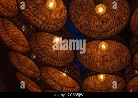 Many wicker lighted lamps hang by background of dark night sky. Lot of hanging electrical lantern, festive decor in evening yard Stock Photo